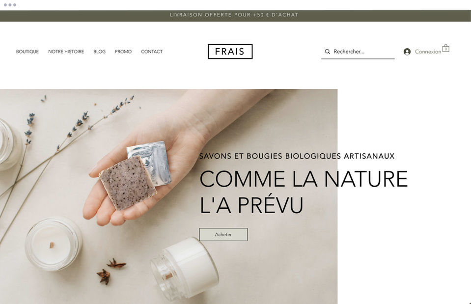 Page d'accueil d'une boutique en ligne de savons et bougies avec une photo de main qui tient 2 savons carrés à côté de 3 petites bougies blance sur un fond beige.